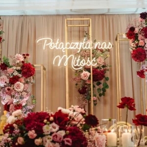 Świecący biały neon LED z napisem Połączyła nas miłość zawieszony na zielonej ściance z roślin